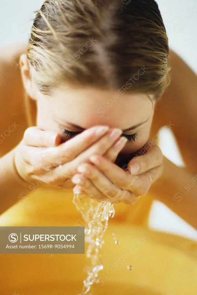 Woman washing face in bathroom sink