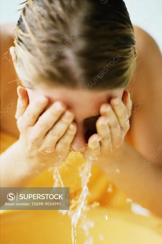 Woman washing face in bathroom sink