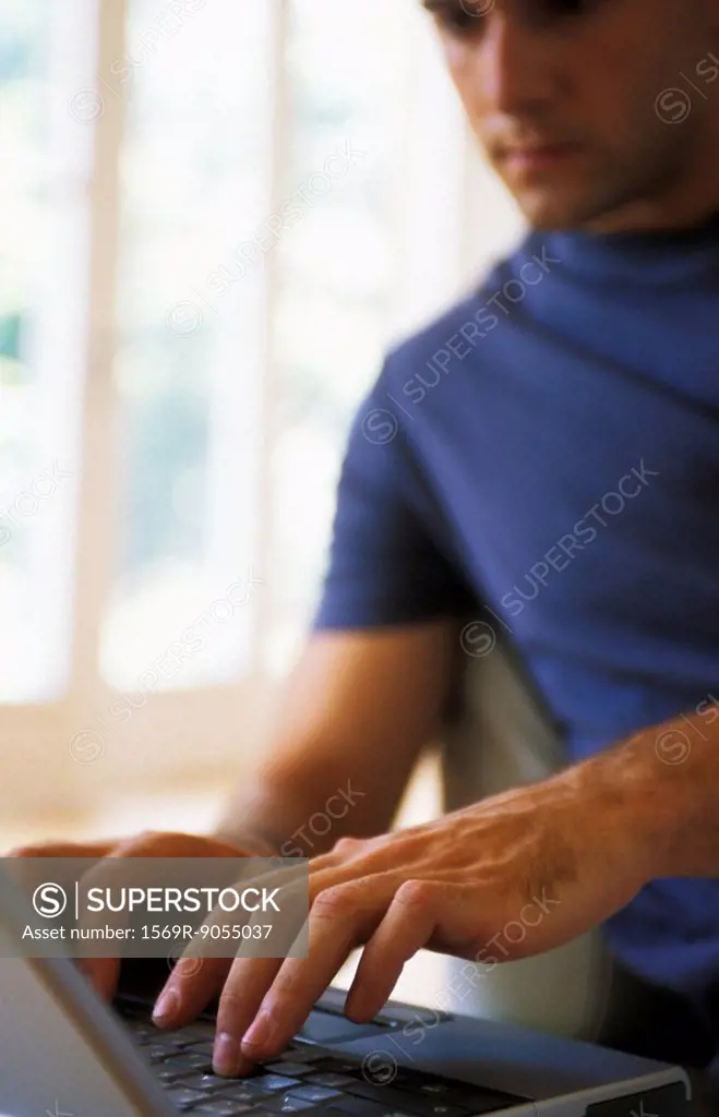 Man typing on laptop, focus on hands