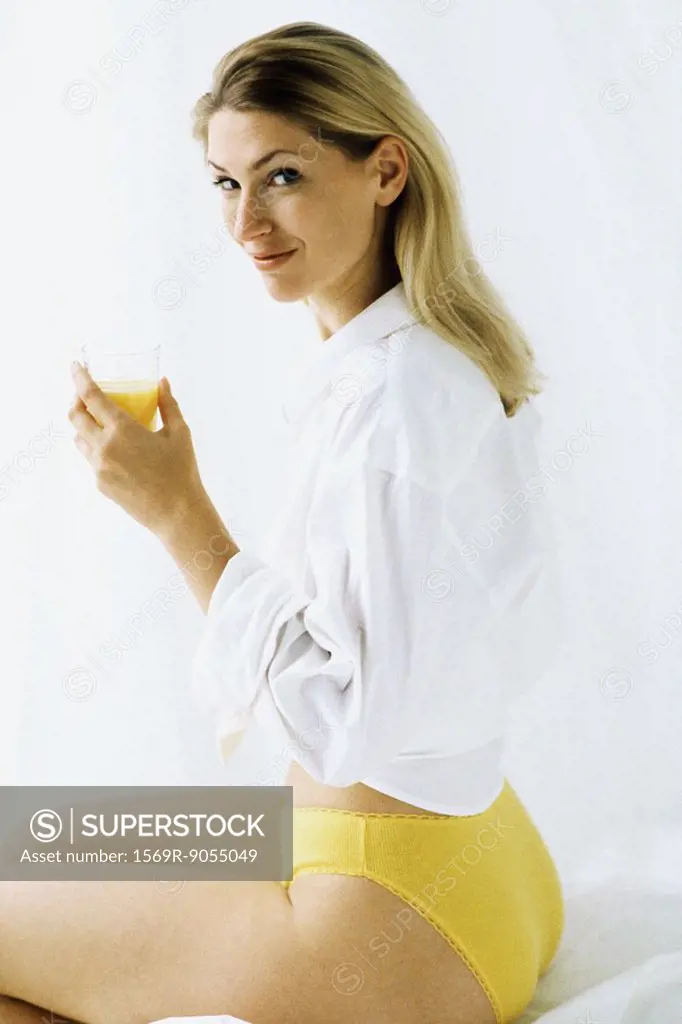 Woman in underwear holding cup of orange juice, smiling over shoulder at camera
