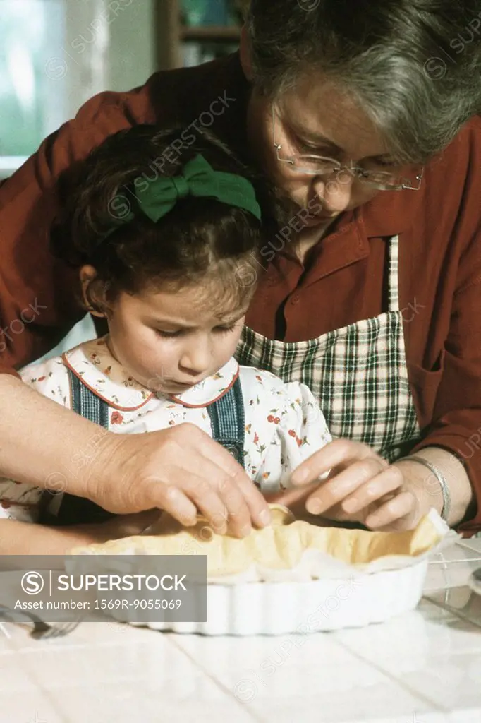 Grandmother preparing pie crust with granddaughter