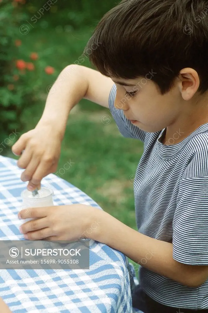 Boy sitting at table, stirring yogurt