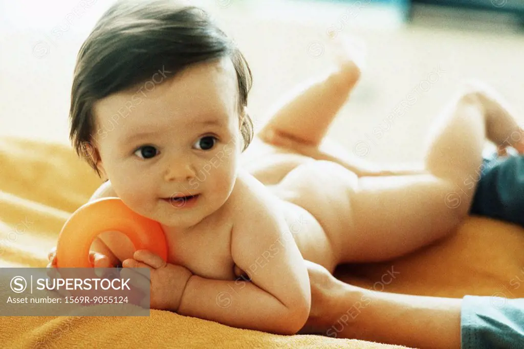 Nude baby lying on stomach, holding plastic ring