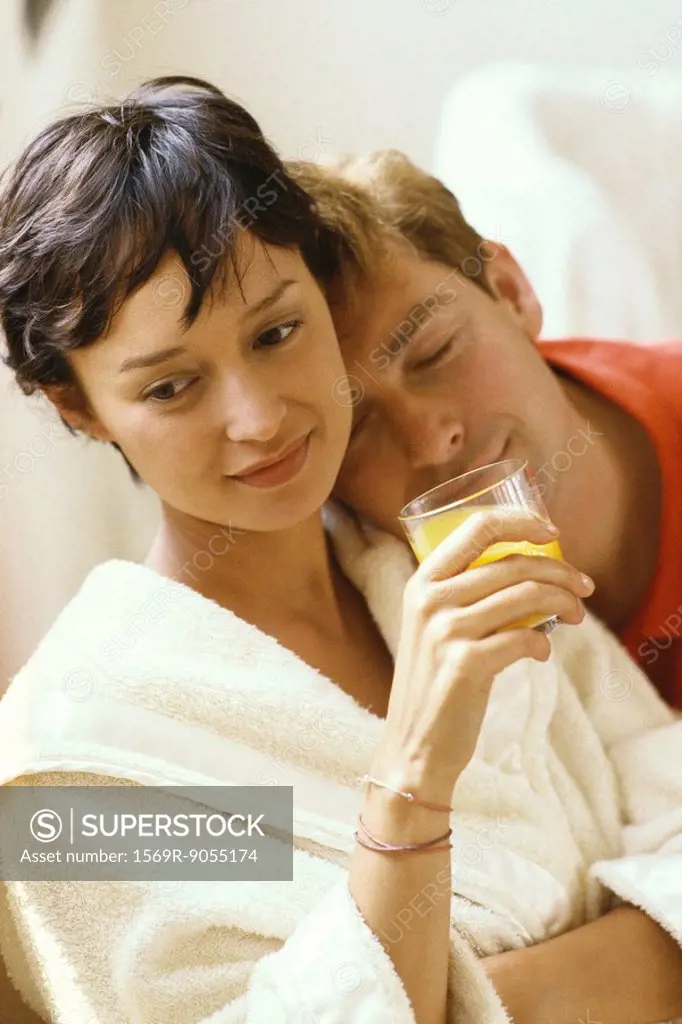 Woman wearing bathrobe and holding glass of juice, man resting head on her shoulder