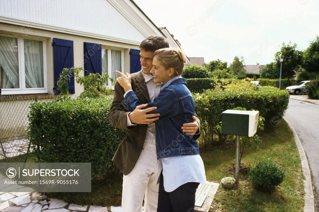 Couple standing in front of house, embracing