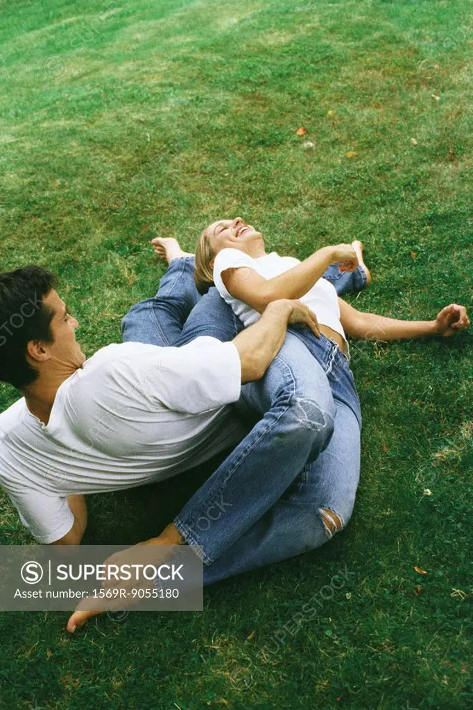 Couple reclining on ground together, laughing, high angle view