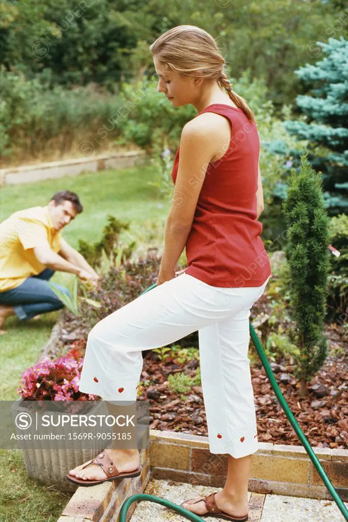 Woman watering garden with hose, husband crouching in background