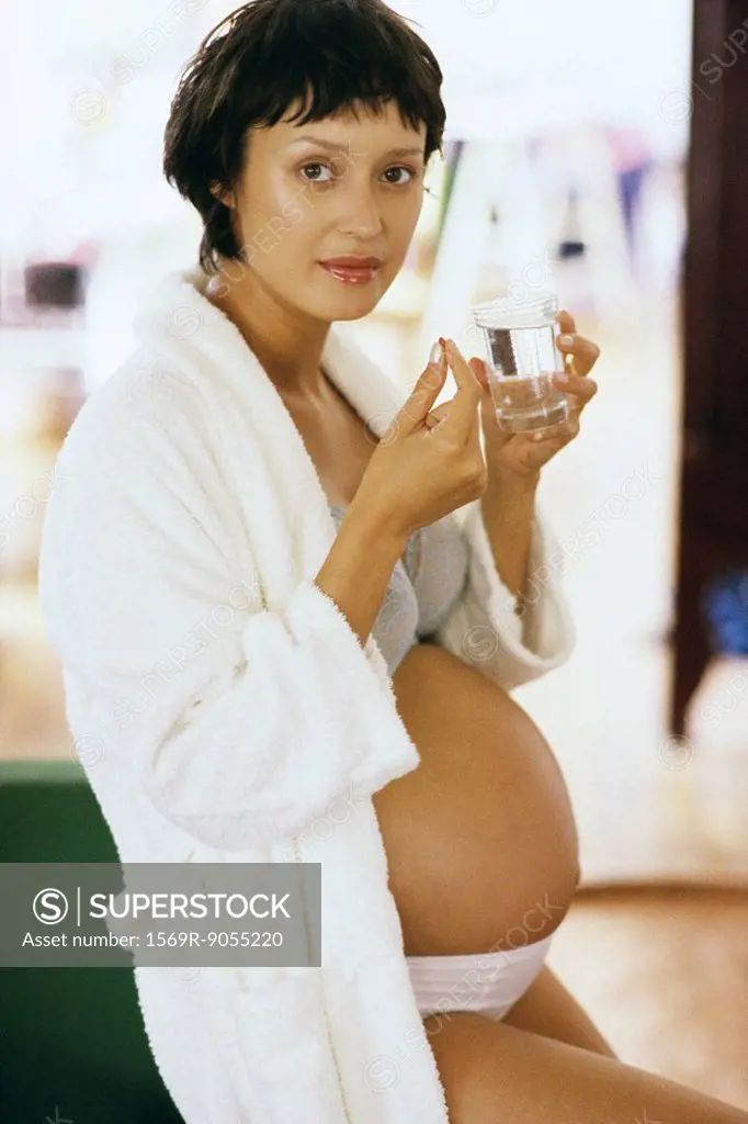 Pregnant woman taking vitamin, looking at camera