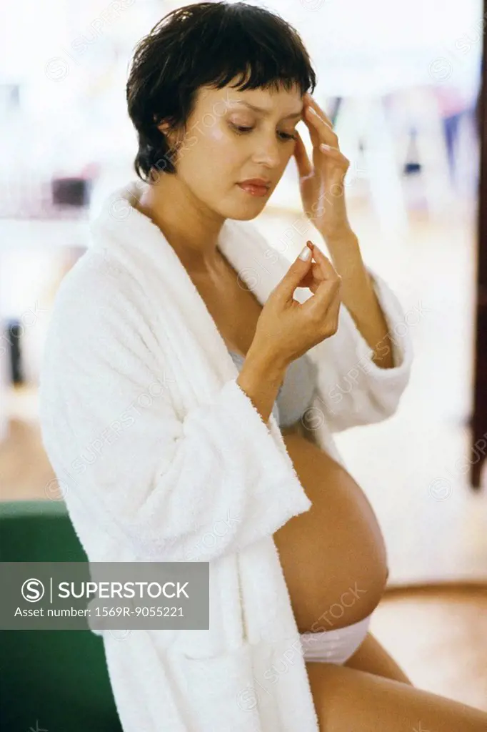 Pregnant woman holding head, looking at pill in hand