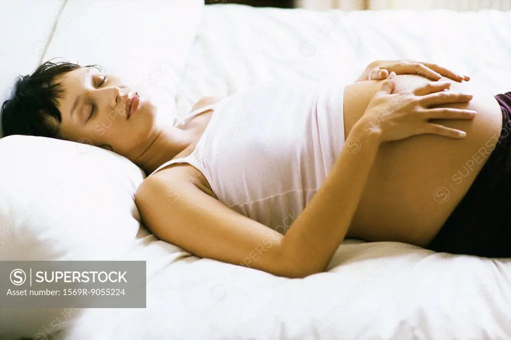 Pregnant woman sleeping on bed, hands on stomach