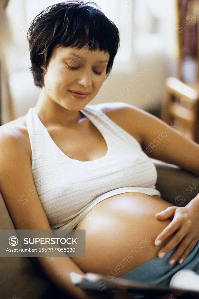 Pregnant woman sitting on sofa, touching her stomach