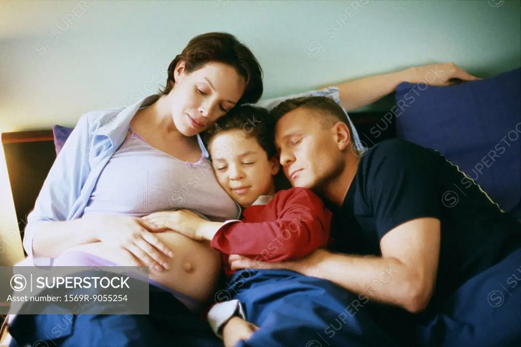 Family together in bed, boy placing hand on woman´s pregnant stomach