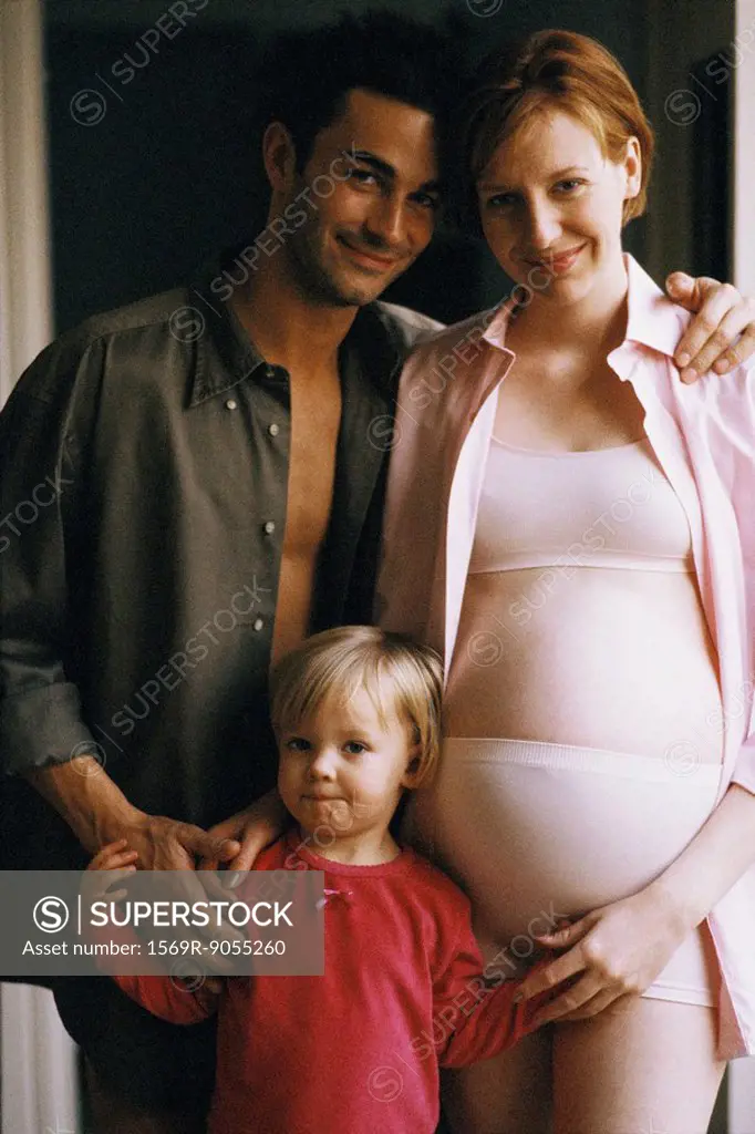 Pregnant woman standing with husband and daughter, smiling at camera