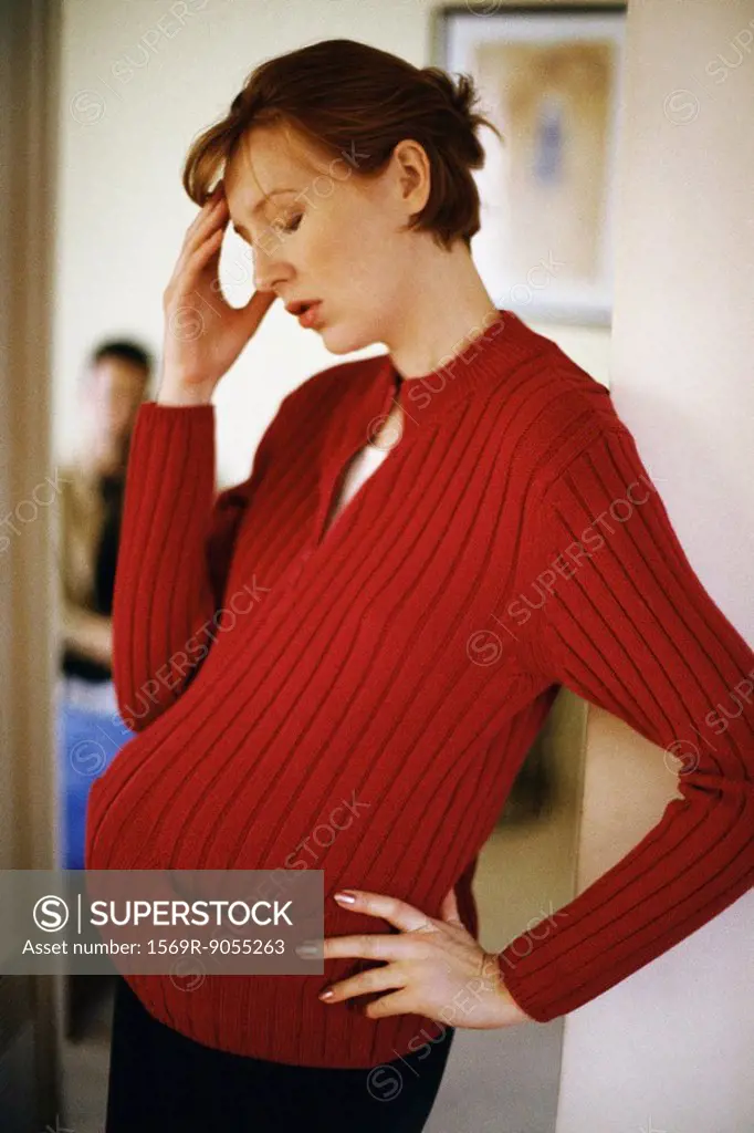 Pregnant woman holding head, man in background
