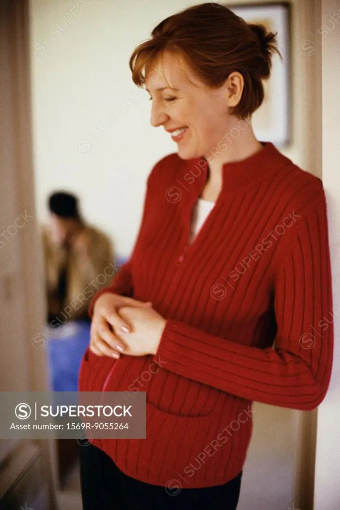 Pregnant woman leaning in doorway with hands on stomach, smiling