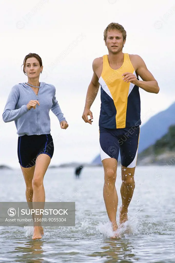 Young couple running together through shallow water near shore