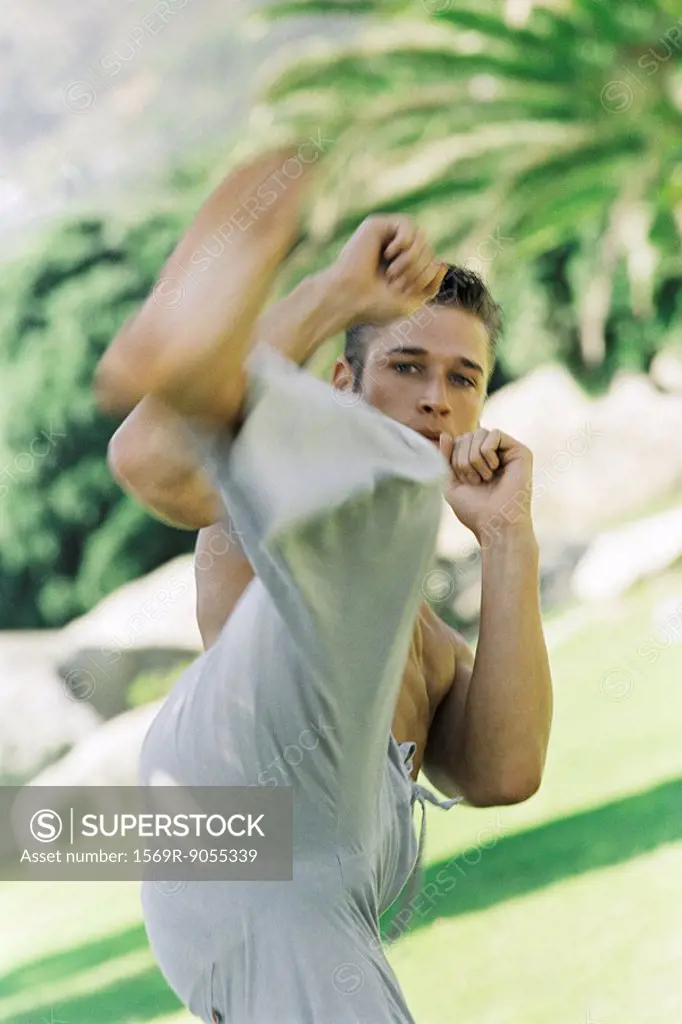 Male practicing martial arts kick in park setting, front view