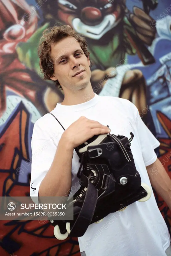 Male with pair of inline skates hanging over shoulder standing in front of wall mural