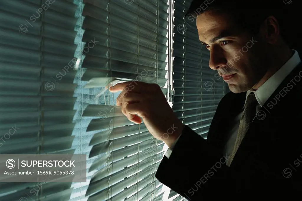 Man in suit discreetly looking through blinds out window