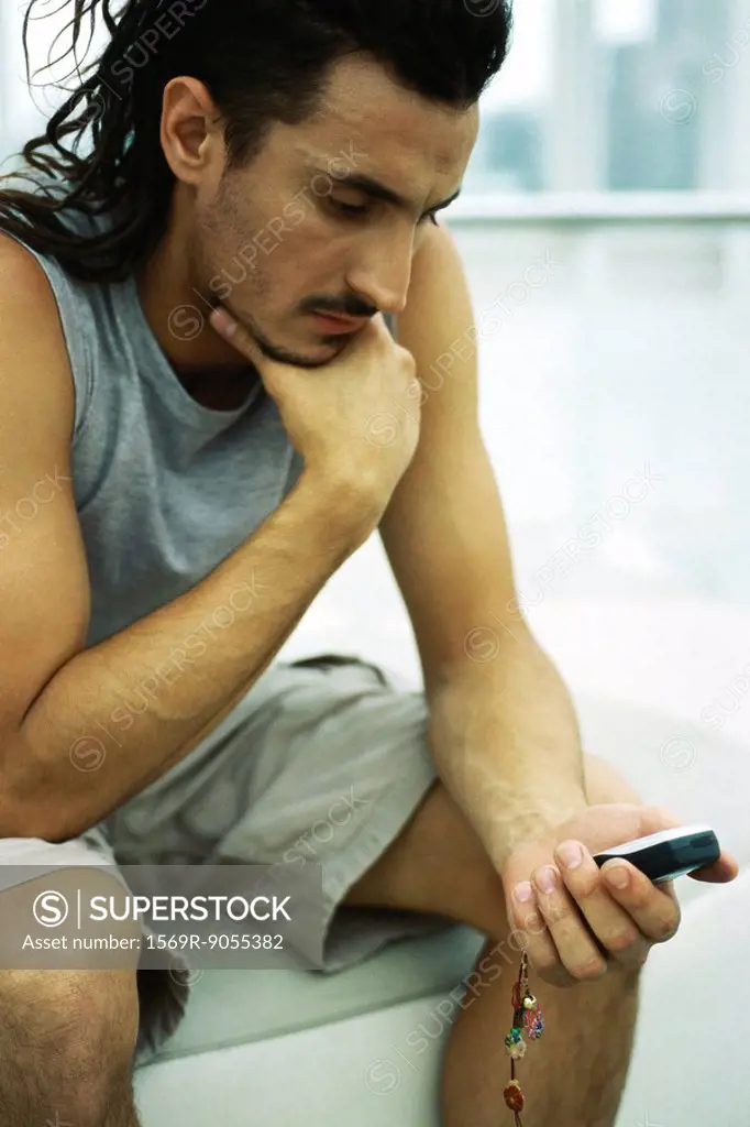 Man sitting with hand under chin, looking at cell phone