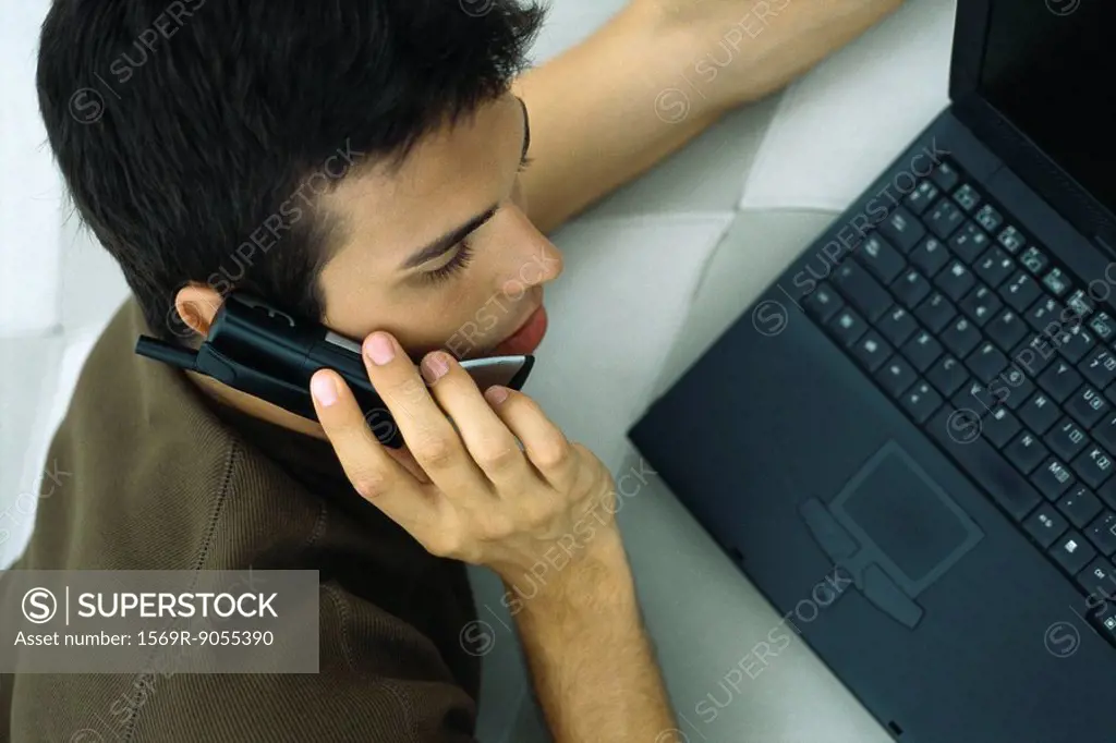 Man phoning, leaning on elbow, using laptop computer