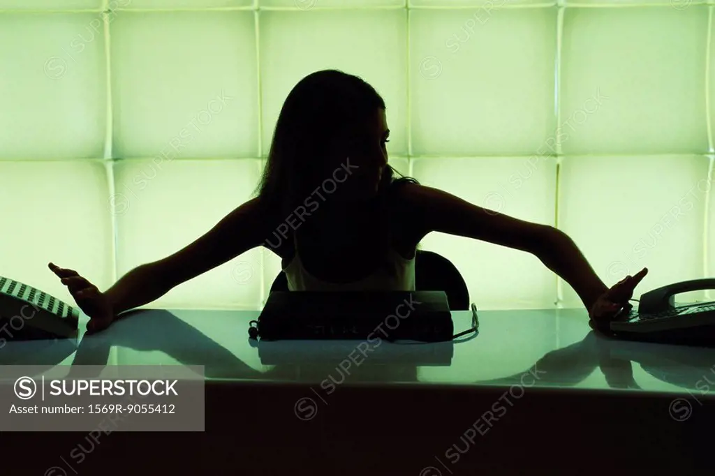 Woman seated at desk reaching for two ringing phones