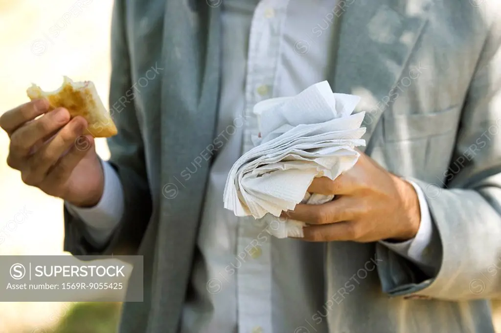 Person holding half eaten pastry in one hand and disposable cup and paper napkins in other hand