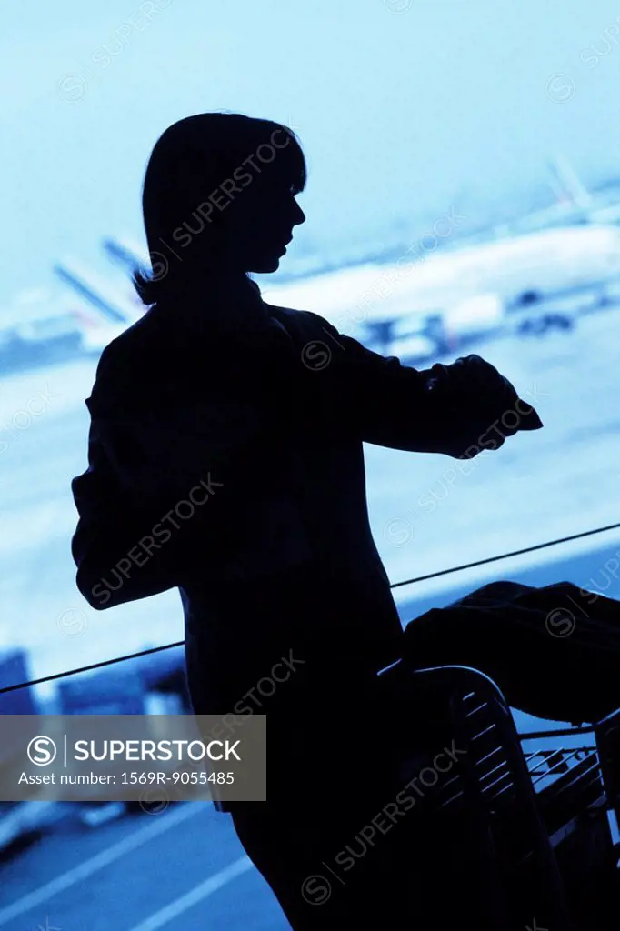 Silhouette of woman traveler looking at watch in airport