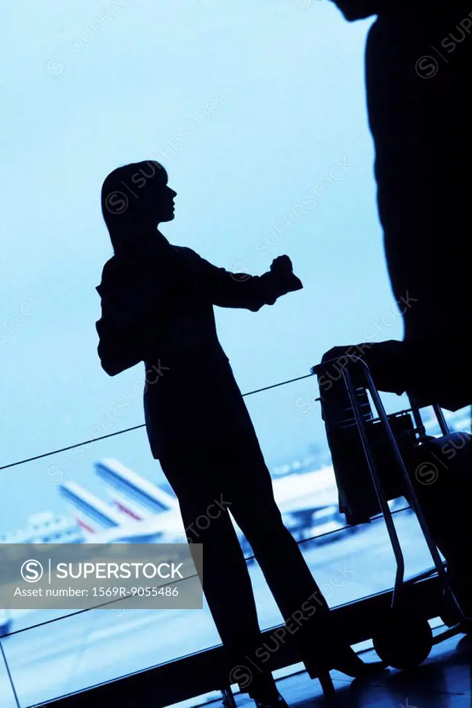 Silhouette of woman traveler standing with luggage cart looking away in airport