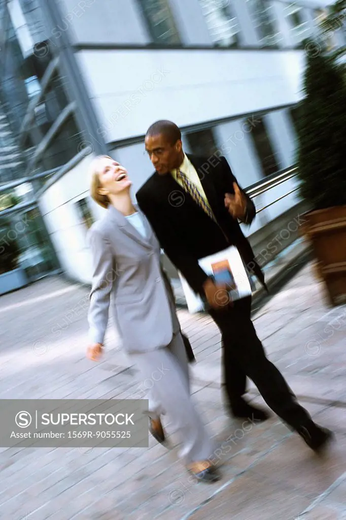 Businessman and businesswoman walking together in conversation, woman laughing