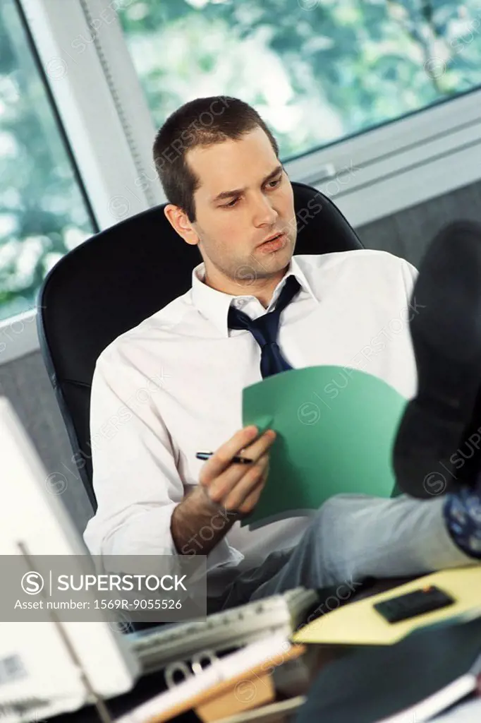 Man with feet up on office desk reviewing document