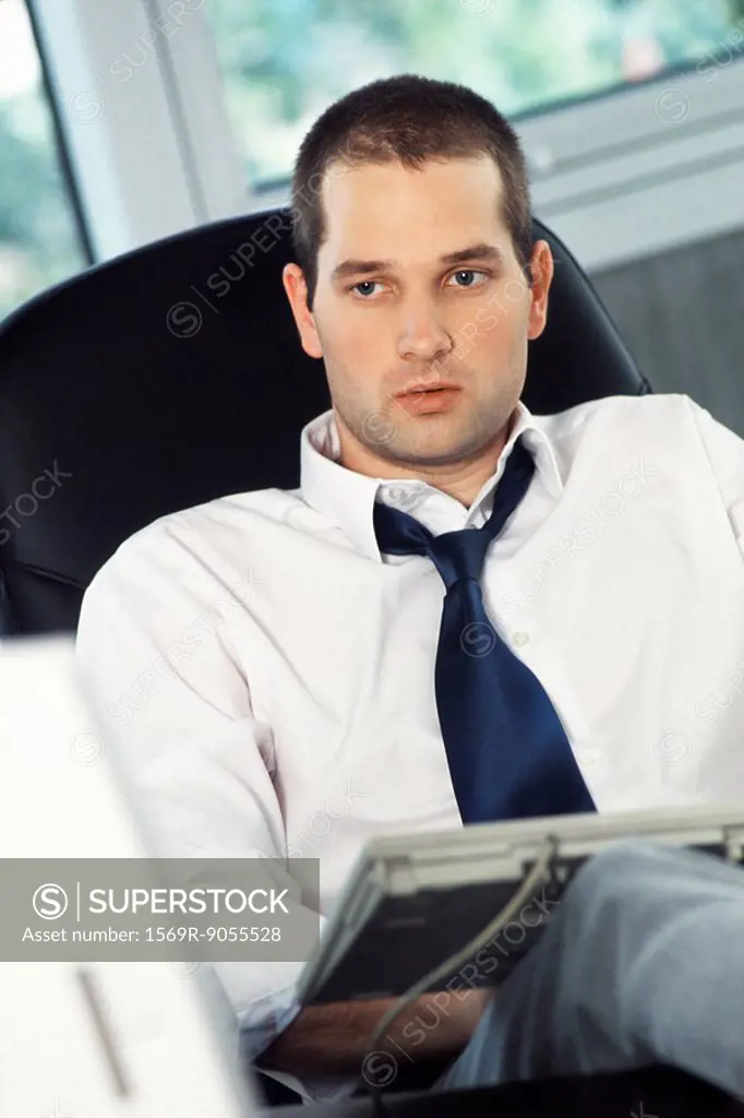 Man with feet up on office desk, typing on computer keyboard set on lap