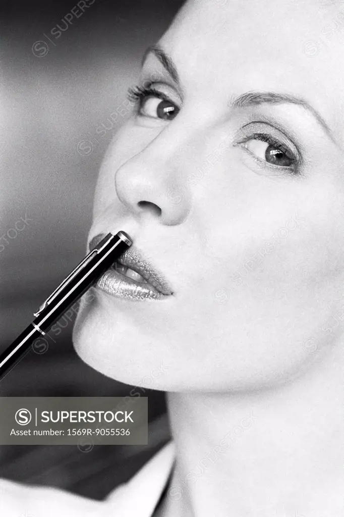 Woman touching lips with pen, glancing sideways at camera