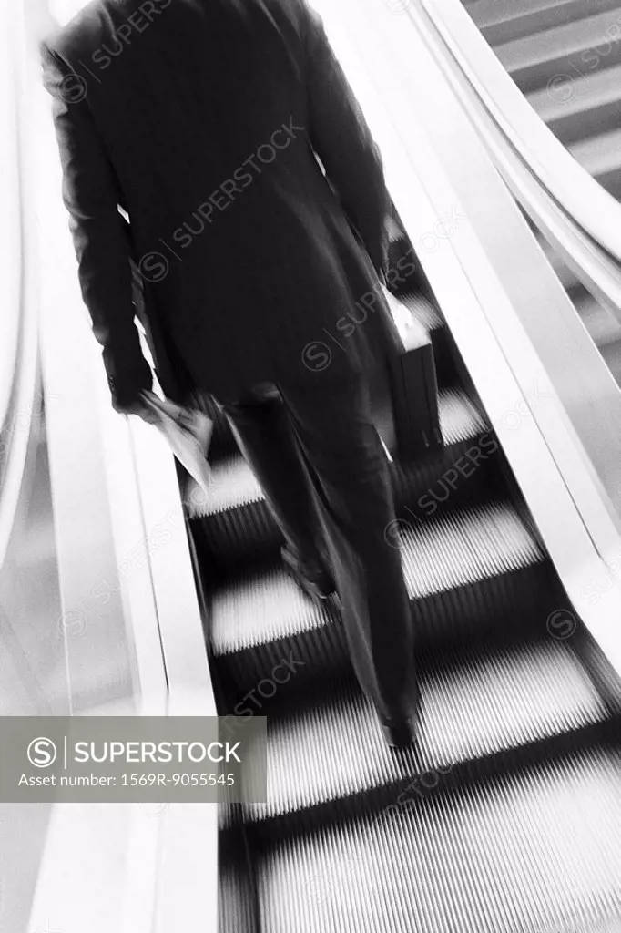 Businessman ascending escalator, rear view
