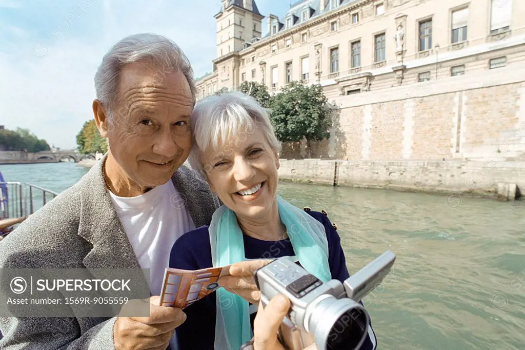 France, Paris, mature couple holding video camera and map, Seine River in background