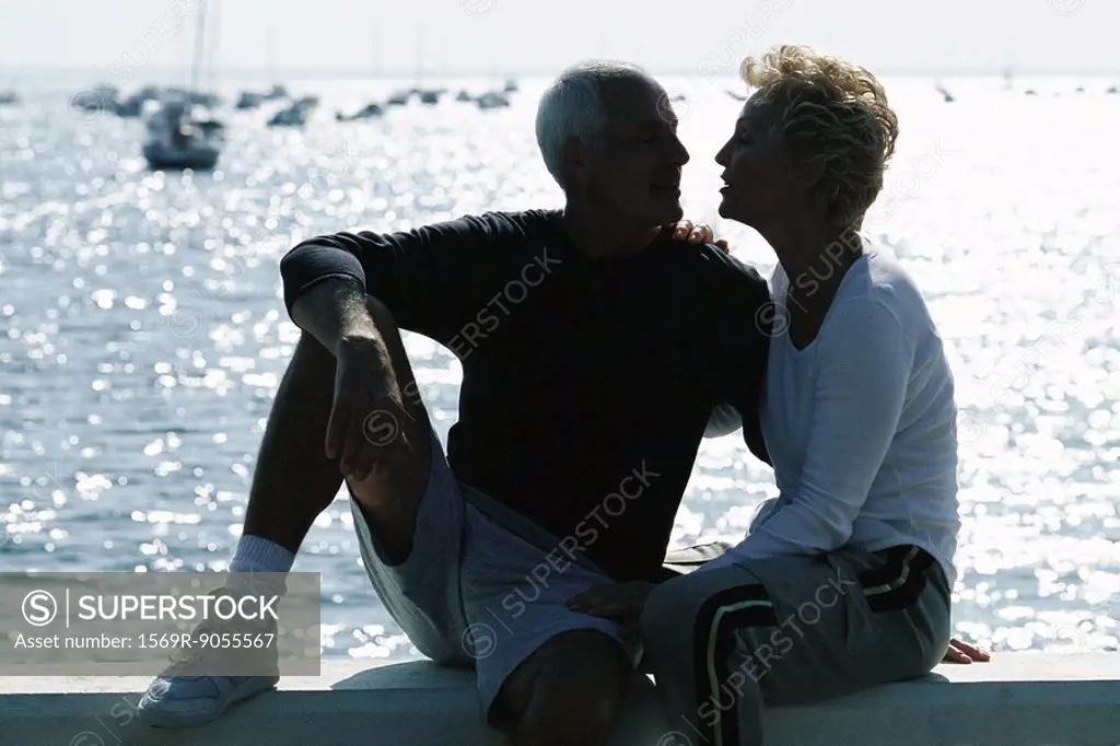 Mature couple sitting together on pier, backlit