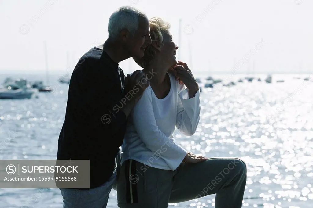 Mature couple standing together on pier, looking at view, backlit