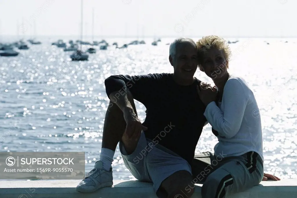 Mature couple sitting together on pier, backlit