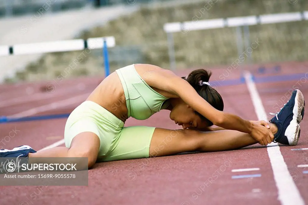 Woman doing stretches on running track, touching forehead to knee