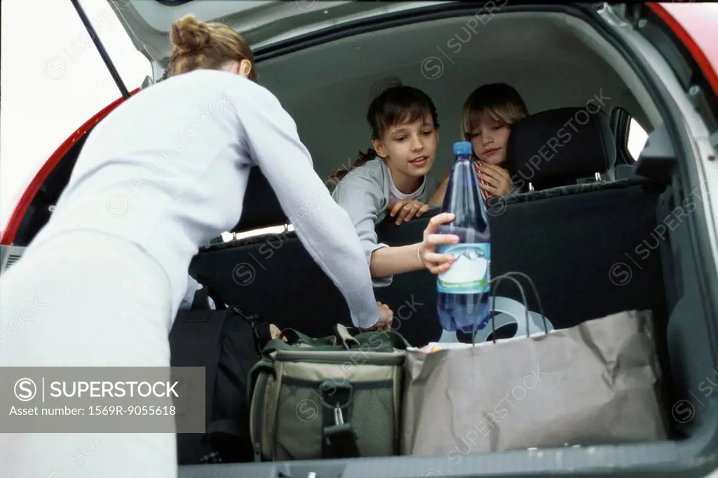 Woman organizing luggage in back of car, children looking over back seat