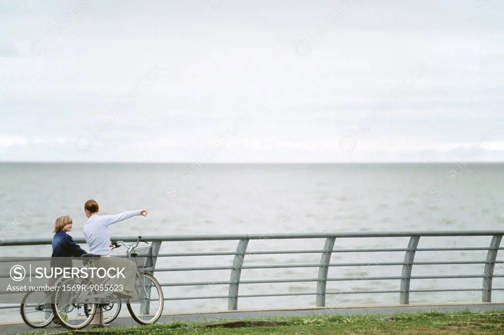 Mother and son on bicycle outing at seaside park, mother pointing to distance