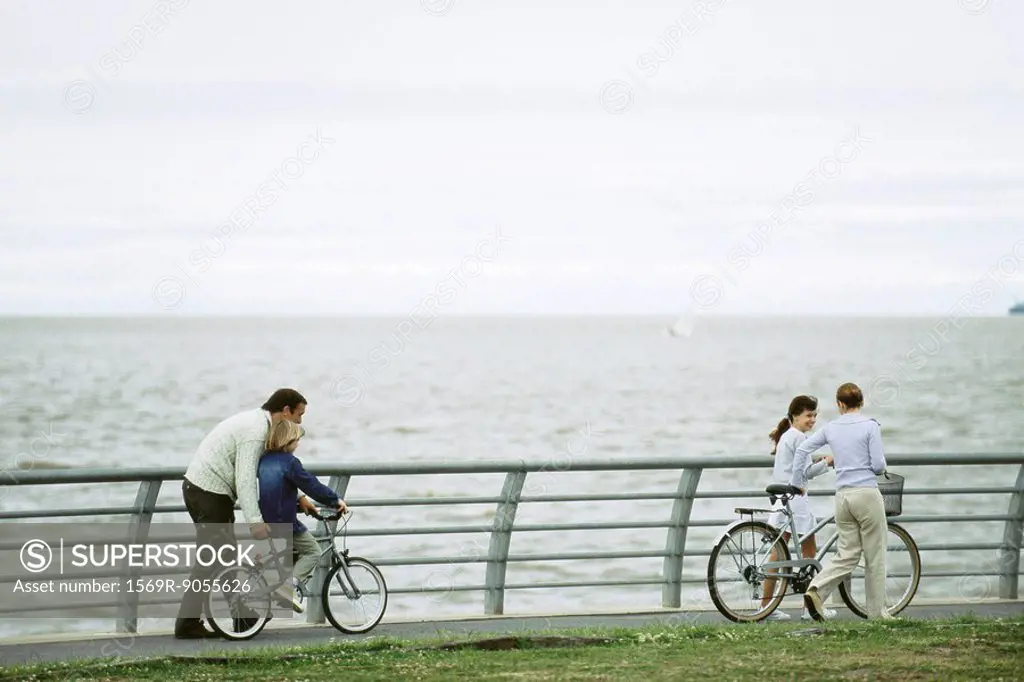 Family riding bicycles together at seaside park, father helping son learn to ride