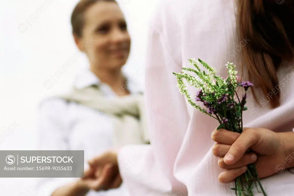 Girl hiding wildflower bouquet behind back, holding mother´s hand, cropped