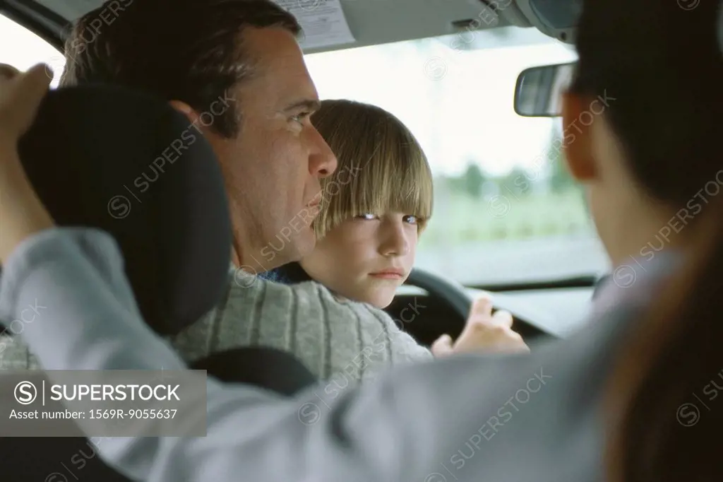 Boy sitting in father´s lap in car, looking over shoulder at sister in back seat