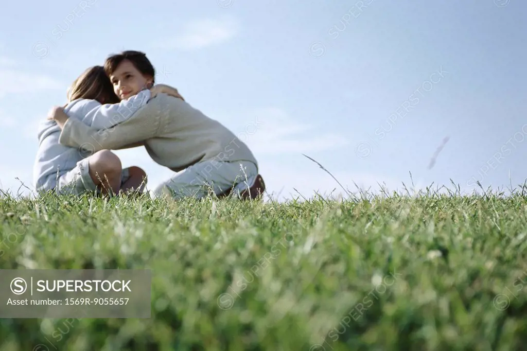 Girl embracing her younger brother in grassy field