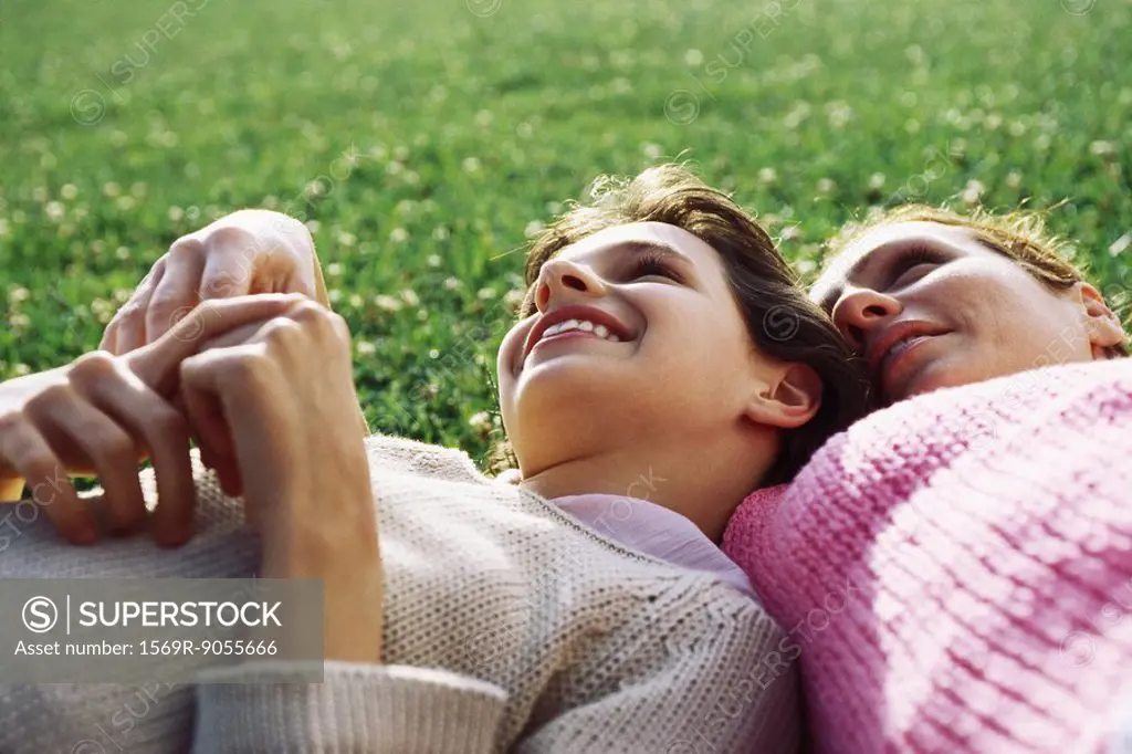 Mother and daughter reclining together on grass, girl resting head on mother´s shoulder