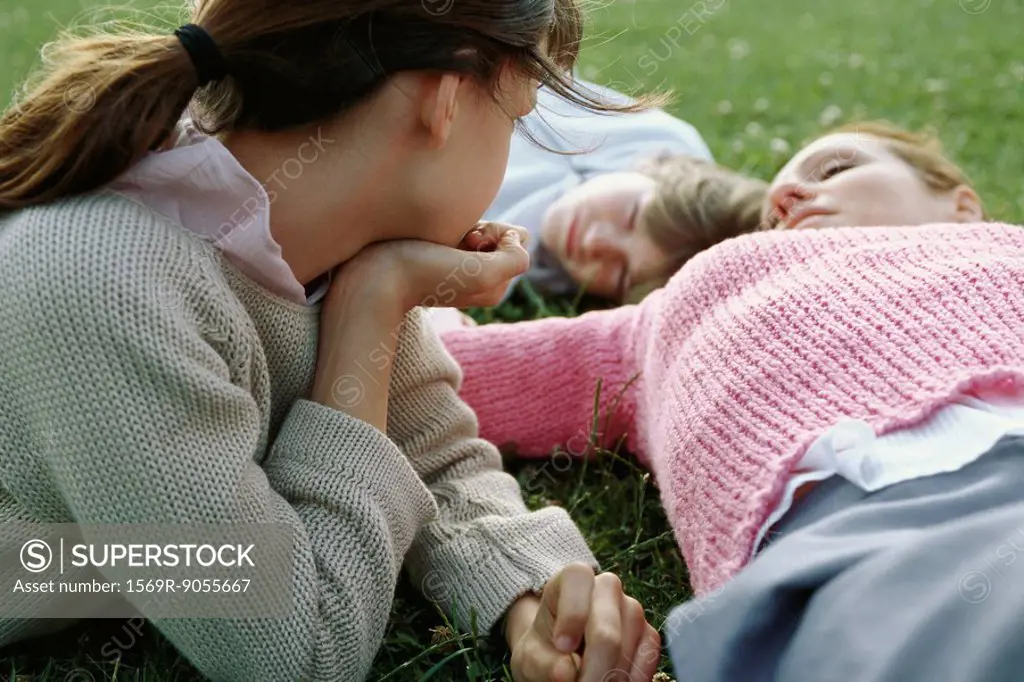 Girl contemplatively observing mother and brother reclining, resting on grass