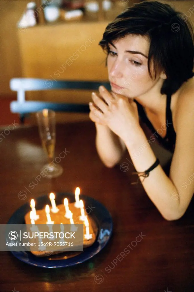 Woman at table with birthday cake looking away wistfully