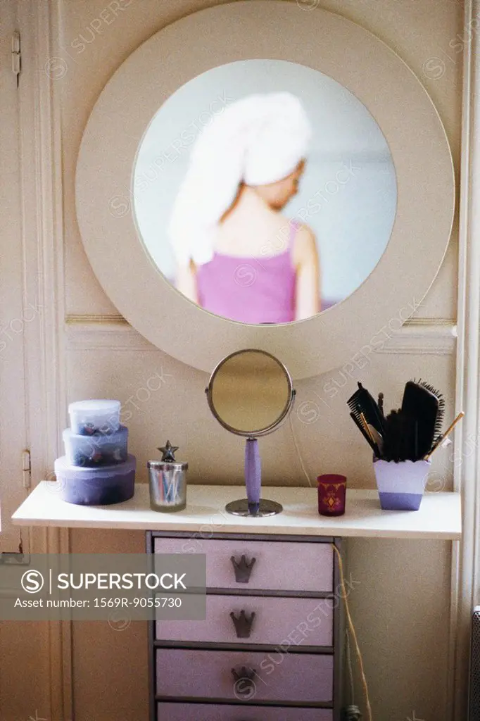 Reflection of woman with head wrapped in towel in mirror hanging above woman´s dressing table