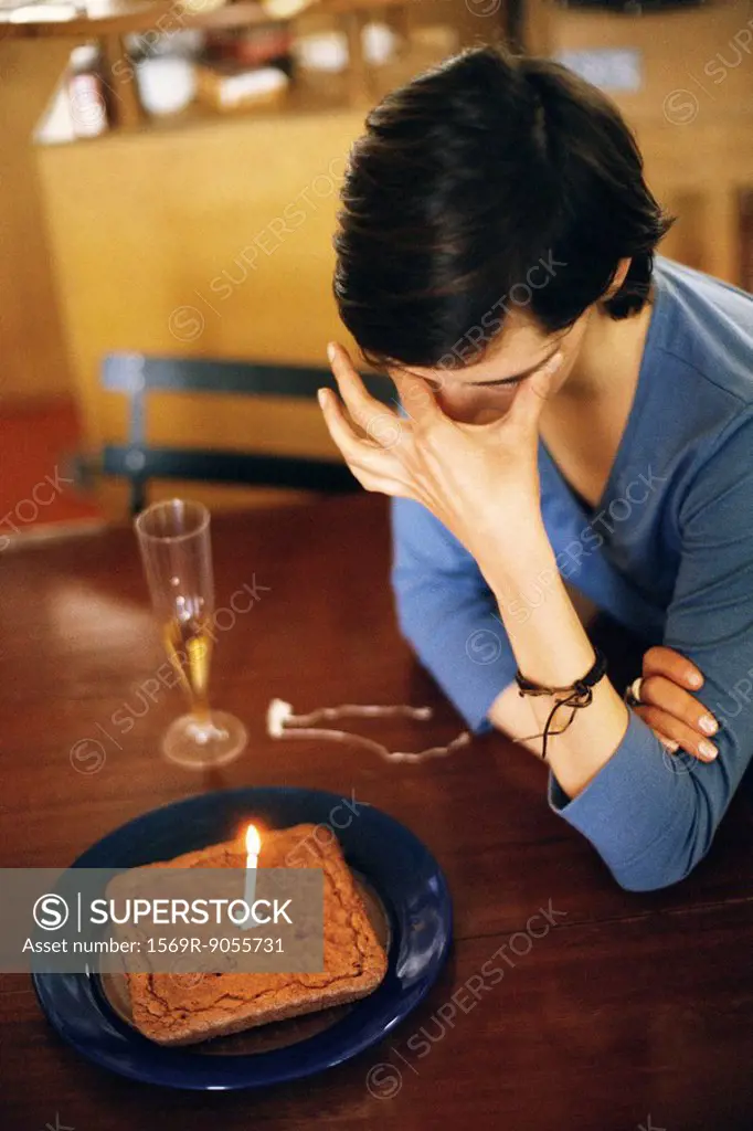 Woman sitting at table alone with anniversary cake, covering eyes